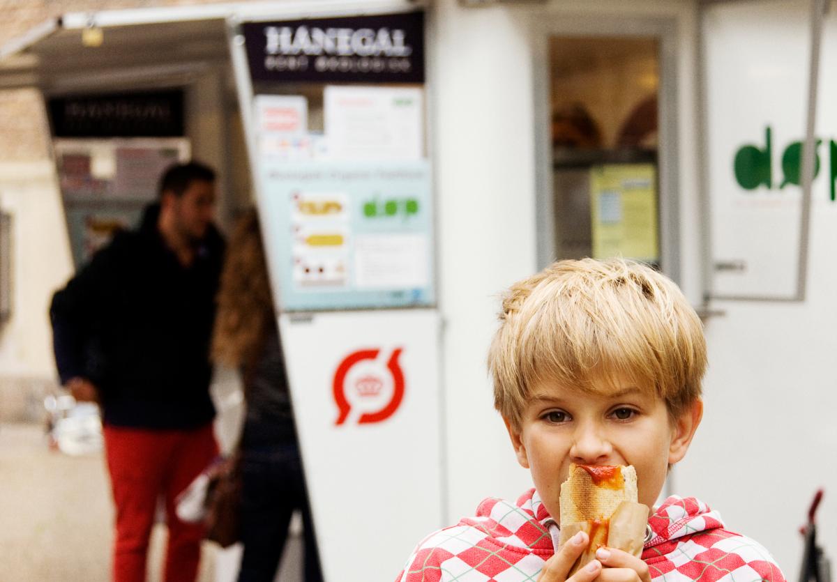 picture of people standing at hotdog stand and young boy eating a hotdog